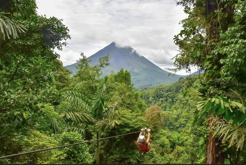 Zip lines run between ridges with Arenal standing behind them.
