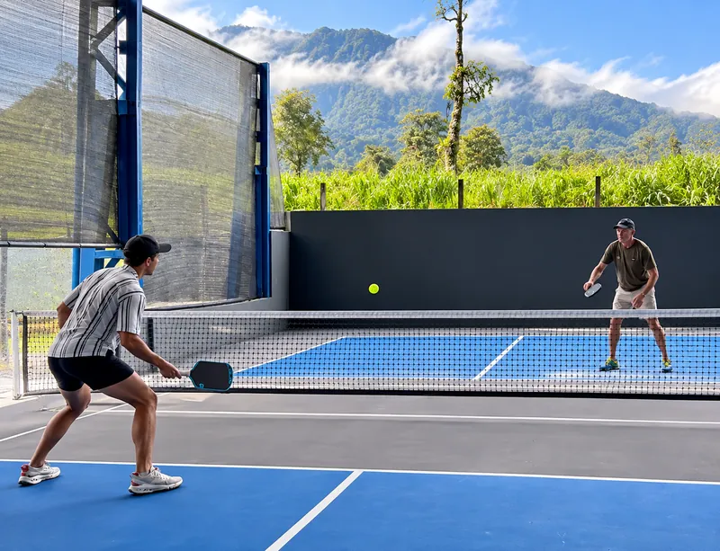 A rally on the covered courts at Volcan Courts Pickleball Club in La Fortuna, with the mountains behind